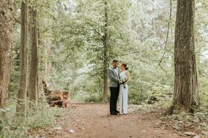 spring wedding photo of the bride and groom. hugs and looks at the bride. forest road between tall trees. Happy wedding couple