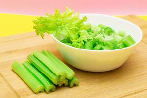 Fresh Chopped Celery Slices in White Bowl with Celery Sticks on Bamboo Cutting Board. Vegan and Vegetarian Culture. Raw Food. Healthy Diet with Negative Calorie Content photo