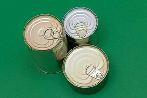 un grupo de apilado estaño latas con blanco bordes en verde antecedentes. Enlatado alimento. diferente aluminio latas para seguro y largo término almacenamiento de alimento. acero sellado comida almacenamiento contenedores foto