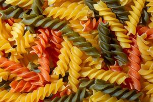 Uncooked Vibrant Colored Fusilli Pasta. A Mesmerizing Culinary Canvas of Multicolored Spirals, Creating a Lively and Textured Background for Gourmet Cooking. Colored Dry Pasta. Raw Macaroni photo