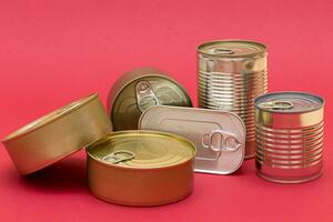 un grupo de apilado estaño latas con blanco bordes en rojo antecedentes. Enlatado alimento. diferente aluminio latas para seguro y largo término almacenamiento de alimento. acero sellado comida almacenamiento contenedores foto