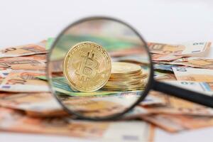 A Stack of Bitcoin Coins Visible Through a Magnifying Glass on the 50-Euro Banknotes. Euro Currency and Crypto Currency. Orange Paper Money. A Lot of Fifty-Euro Bills. Anonymous Payments Concept photo