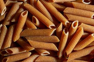 Uncooked Whole Grain Penne Rigate Pasta. A Culinary Canvas of Whole Wheat Macaroni, Creating a Lively and Textured Background for Gourmet Cooking. Whole Grain Dry Pasta. Whole Wheat Raw Macaroni photo