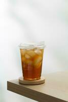 con hielo té en un claro el plastico vaso en un de madera mesa con un blanco antecedentes. foto