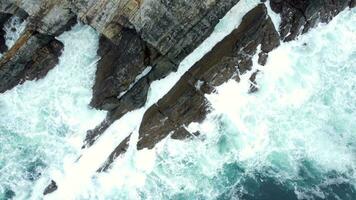 Haut aérien vue de océan vagues éclaboussures contre rochers Contexte. caméra dans inclinaison vers le bas position. drone lentement Ascendant. spectaculaire Naturel phénomène. video