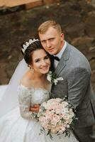 Wedding photo. The bride in a voluminous white dress and a long veil stands with the groom in the park on a stone path. View from above. Portrait of the bride. Beautiful curls. Beautiful makeup. photo