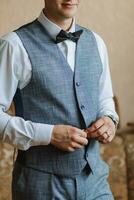 Morning of the groom and details, white shirt, blue vest, good light, young man, stylish groom getting dressed, getting ready for the wedding ceremony. close-up of male hands photo