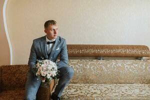 groom with a bouquet of flowers in a room with a wonderful interior. Groom looking left, space for signature or advertisement photo