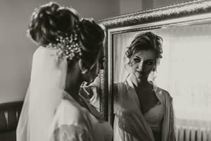 A blonde bride in a long, lacy petticoat is standing in her room, posing by the mirror, putting on her earrings. Beautiful hair and makeup, open bust. Wedding portrait. Reflection in the mirror photo