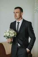 Portrait. A man in a white shirt, black bow tie and black tie poses in a room with a wedding bouquet. A stylish watch. Men's style. Fashion. Business photo