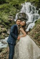 Portrait of a happy bride and groom near a waterfall. Bride and groom. Wedding photo session in nature. Photo session in the forest of the bride and groom.