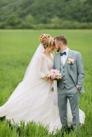 The newlyweds stand in a green field and kiss. The bride is holding a bouquet. Wedding in nature. Portrait of the bride and groom. Stylish groom photo