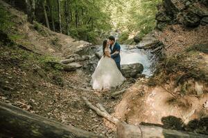 Wedding couple is hugging near the mountain river. Groom and bride . Nature wedding photoshoot. Photo session in the forest of the bride and groom.