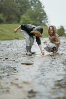 dos contento pequeño muchachas de europeo apariencia jugando en charcos durante lluvia en verano. niños son jugando en el lluvia. niño jugando en naturaleza al aire libre. el niña disfruta el lluvia. foto
