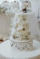 White wedding cake with flowers. Beautiful homemade three-tiered wedding cake decorated with white orchids in a rustic style on a white table photo