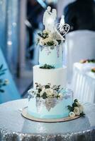 A blue and white wedding cake, decorated with flowers and silver, stands on a silver stand. Decoration in the form of brides. flowers Wedding. Sweets photo