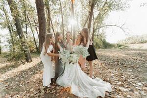 Wedding photo in nature. The bride and her bridesmaids are standing in the forest smiling, holding their bouquet and looking at the bride. Happy wedding concept. Emotions. girls