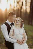 Wedding photo in nature. The groom sits on a wooden stand, the bride stands next to him, leaning on his shoulder. look at each other. Portrait of the bride and groom