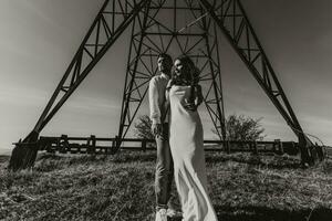 Stylish model couple in the mountains in summer. A young boy and girl in a white silk dress are standing near large structures of power lines. Black and white contrast photo