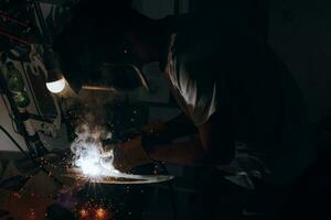 A welder is doing welding work in his garage while sparks fly around, he is wearing a safety helmet. Manual work with a welding device photo