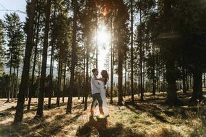 elegante modelo Pareja en blanco ropa besos a puesta de sol en el bosque. un niña abrazos su marido, pelo soplo en el viento. amplio ángulo foto