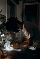 A welder is doing welding work in his garage while sparks fly around, he is wearing a safety helmet. Manual work with a welding device photo