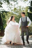 Groom and bride in the garden. Spring wedding in the park. Happy wedding couple running in the park. Stylish and beautiful. Princess dress. photo