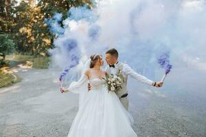 en su manos, el recién casados sostener multicolor fumar bombas de azul color. novio y novia beso. Boda divertida. foto