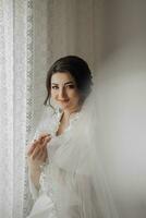 Portrait of a brunette bride touching her face. Gorgeous make-up and hair. Voluminous veil. Wedding photo. Beautiful bride photo