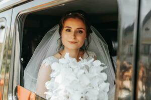 the bride sits in a black car on the wedding day with a bouquet. Portrait of the bride. lush white lace dress photo