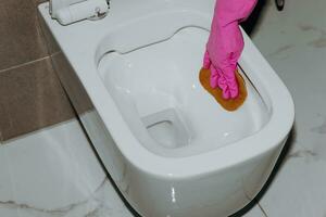 a woman cleans the toilet with a toilet tissue. A housewife as a toilet cleaner. Clean the toilet for cleanliness and hygiene. toilet cleaning Cleaning service concept. Pink rubber glove photo