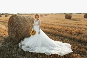 Wedding portrait. A red-haired bride in a white dress, holding a bouquet of sunflowers, on the background of a field. Beautiful curls. Sincere smile. Elegant dress. Yellow flowers photo