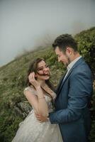 Happy wedding couple in the mountains. The bride with her long hair blowing in the wind smiles sincerely. Wedding photo session in nature. Photo session in the forest of the bride and groom.