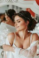 tall bride with bare shoulders, open bust, in a room near a mirror. Great wedding hairstyle. lace robe. Portrait. Delicate wedding makeup photo