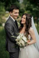 Happy young couple. Wedding portrait. The bride and groom smile sincerely. Young people are tenderly hugging while looking at the camera. Wedding bouquet. Spring wedding photo