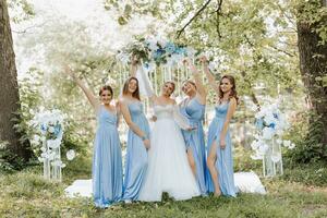 The bridesmaids in blue dresses raise their hands, rejoice, the bride is holding a beautiful bouquet. Beautiful luxury wedding blog concept. Spring wedding. photo