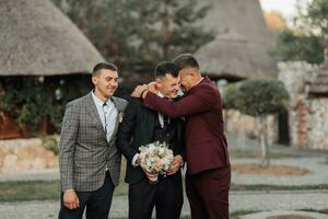 Photo of three men in classic suits. A man holds a bouquet while standing among his friends. Business style. Stylish men