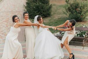 Boda foto en naturaleza. un morena novia en un blanco largo vestir y su amigo en un desnudo vestir son engañando alrededor juntos y sonriente atentamente. joven mujer. emociones