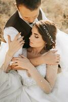 retrato de un elegante novio con un novia en un antecedentes de otoño seco césped. el concepto de un rural Boda en el montañas, contento bohemio recién casados. el novia y novio son acostado en el césped foto