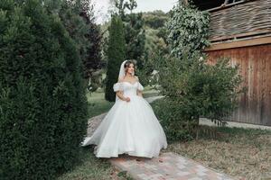 Wedding photo. The bride in a voluminous white dress and a long veil walks in the garden along a stone path. View from above. Portrait of the bride. Beautiful curls. Beautiful makeup and hair. photo