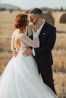 Wedding portrait of the bride and groom standing hugging and leaning their noses against each other. Red-haired bride with open shoulders. Stylish groom. Summer photo