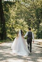 Groom and bride in the garden. Spring wedding in the park. Happy wedding couple running in the park. Stylish and beautiful. Photo from the back. Princess dress.