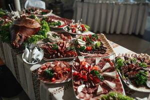 Buffet table at the wedding. An assortment of snacks on white plates standing on a Ukrainian-style tablecloth. Banquet service. Food, snacks with cheese, ham, prosciutto and greens. photo