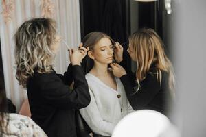 The face of a beautiful young woman. The process of creating hair and makeup. Beautiful hands in the process of work. White and black clothes. Three women with blond hair photo