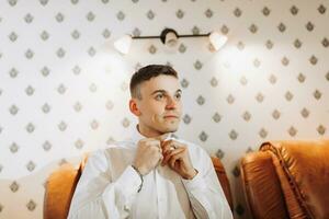 Mañana de el novio y detalles, blanco camisa, bueno luz, joven hombre, elegante novio consiguiendo vestido, consiguiendo Listo para el Boda ceremonia. de cerca de masculino manos, foto