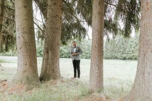 elegante acicalar, propensión su hombro en contra un árbol, enfatiza su barba, mira dentro el cámara lente. retrato foto