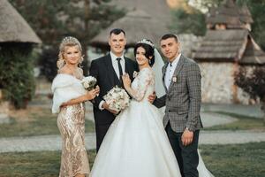 frente ver de recién casados caminando mano en mano entre amigos. muchachas en dorado vestidos sostener ramos de flores, el novia en un voluminoso vestido, el novio y su amigos en trajes. Boda en naturaleza foto