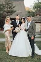 Front view of newlyweds walking hand in hand among friends. Girls in golden dresses hold bouquets, the bride in a voluminous dress, the groom and his friends in suits. Wedding in nature photo