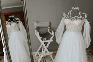 A perfect wedding dress with a magnificent skirt on a mannequin. Reflection in the mirror. A stylish chair on the background photo