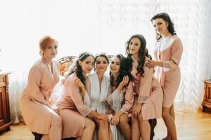 Bridesmaids have fun with the bride. The bride and her fun friends are celebrating a bachelorette party on a retro sofa in matching robes. Bride and friends in the room photo